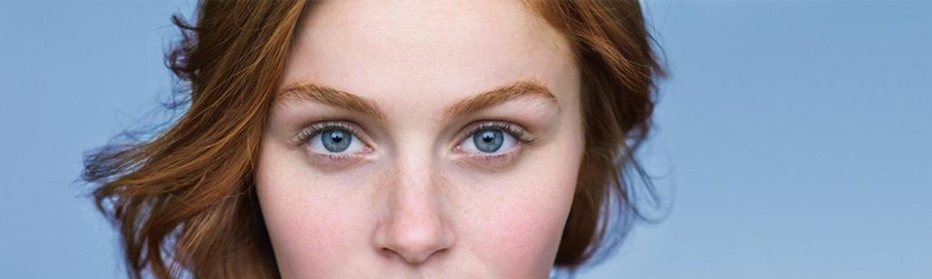 En rødhåret kvinne med blå øyne og synlig rødme i kinnene, typisk for hud med tendens til rosacea